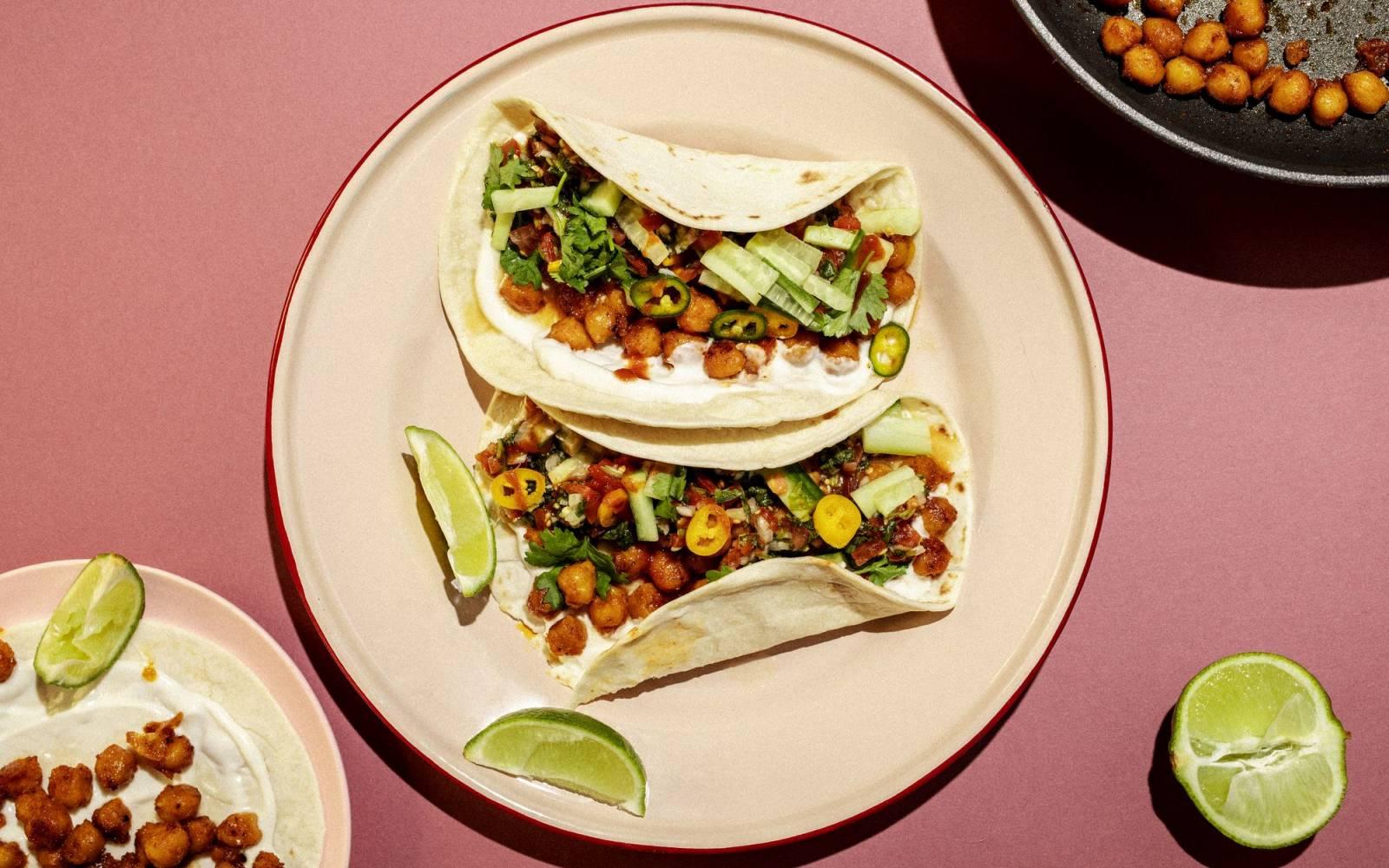 Teller mit veganen Tacos mit Kichererbsen auf rosa Tischplatte